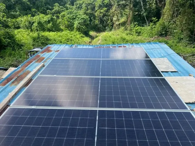 Solar panels on a roof at an off-grid site surrounded by forest in Sarawak